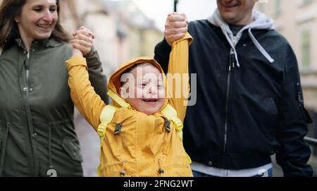 Feliz familia con síndrome de Down hijo al aire libre en un paseo bajo la lluvia, divertirse.