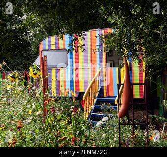 Corps-Nuds, Francia. Ille y Vilaine departamento.. El colorido jardín reúne una vieja caravana pintada con líneas de colores, rodeada de muy c Foto de stock