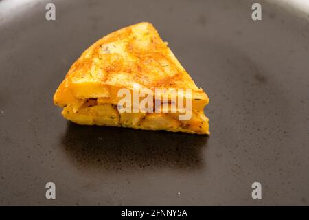 Vista de cerca normal de una porción de patata casera o tortilla de papa en un plato negro sobre una mesa de mármol claro. Concepto de tapas tradicionales. Foto de stock
