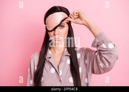 Foto de disgustada linda mujer joven ropa de dormir mano mascarilla para el brazo cubra el ojo con fondo de color rosa aislado