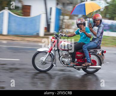 Los hombres de Sri Lanka viajan en moto llevando paraguas bajo lluvia torrencial (tomada con la técnica de cámara 'panorámica'), Bahía de Arugam, Provincia Oriental, Sri Lanka Foto de stock