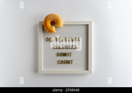 Letterboard con palabras que se espetan los fines de semana Calories Donut Contar, en letras doradas, con un donut fresco, sobre un fondo blanco, horizontal Foto de stock