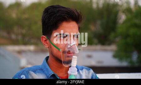 Hombre asiático infectado con la enfermedad de Covid 19. Paciente indio que respira oxígeno usando máscara solo en su casa. Niño adulto inhalar con nebulizador para tratantes