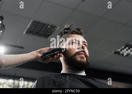 Corte de pelo de máquina de bajo desvanecimiento para hombre guapo con barba  en peluquería. corte de pelo con transición suave.