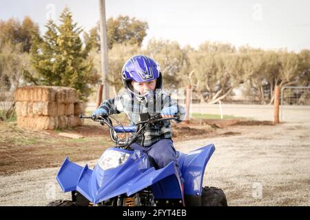 Un ni o peque o en un casco azul que conduce el ATV o en quad