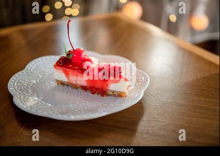 Un trozo de tarta de queso de fresa con capa de galletas, cereza y mermelada en plato blanco en el restaurante Foto de stock