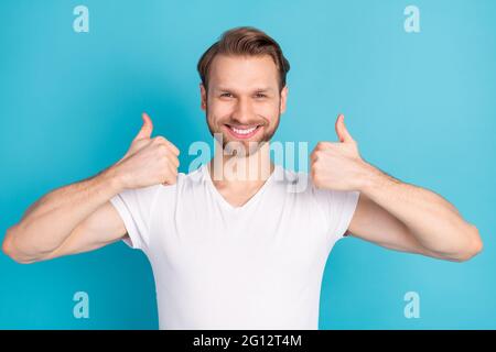 Retrato de un joven simpático y satisfecho le disparó dos pulgares hacia arriba sonriendo aisladas sobre fondo de color azul Foto de stock