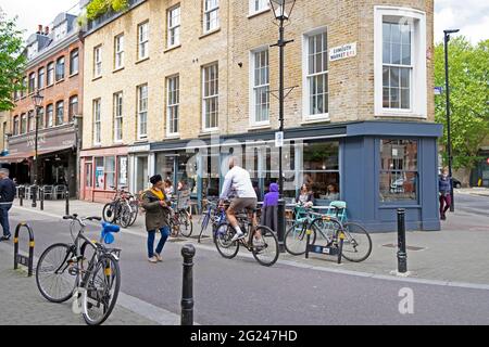 Gente paseando en bicicleta fuera del restaurante Briki y el cartel de la calle Exmouth Market en el edificio en Clerkenwell Islington Londres EC1 Inglaterra Reino Unido KATHY DEWITT Foto de stock