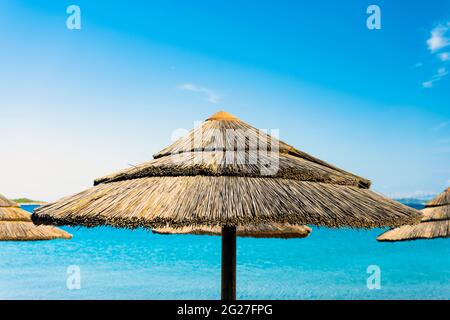 (Enfoque selectivo) Vista impresionante de un paraguas de paja en primer plano y hermoso mar turquesa en el fondo. Cerdeña, Italia. Foto de stock