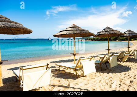 (Enfoque selectivo) Vista impresionante de algunas sombrillas y tumbonas en una playa bañada por un hermoso mar turquesa. Cerdeña, Italia. Foto de stock