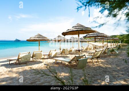 (Enfoque selectivo) Vista impresionante de algunas sombrillas y tumbonas en una playa bañada por un hermoso mar turquesa. Cerdeña, Italia. Foto de stock