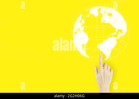 Concepto de tecnología multimedia mundial. Dedo de la mano de la mujer joven apuntando con holograma sobre fondo amarillo. Concepto de negocio internacional Foto de stock