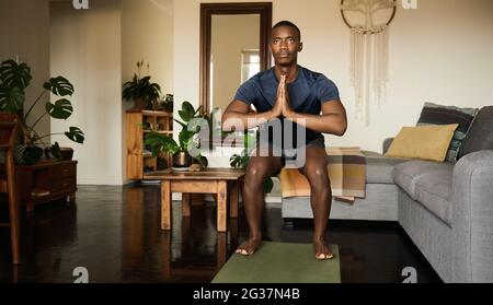 El hombre africano en la silla pose mientras hace yoga en casa