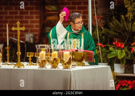 Un sacerdote asiático-americano se deshace de su gorra en una misa por el reconocimiento de los miembros de Vida Consagrada y Jubilares en una iglesia católica de California. Foto de stock