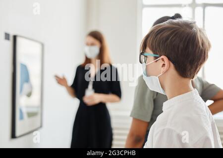 Vista lateral del grupo de niños mirando las pinturas en la galería de arte y usando máscaras, espacio de copia