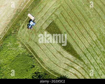 drone tiro de tractor azul con cortacésped cortando prado verde fresco en alguna parte en austria Foto de stock