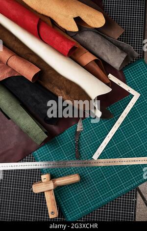 Muestras de cuero auténtico de diferentes colores se enrollan sobre una mesa con esteras y herramientas para cortar piezas de cuero, un taller de costura de correa Foto de stock