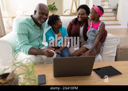 Feliz abuelo afroamericano y abuela en sofá con nietos mirando el portátil Foto de stock