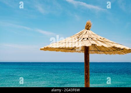 Una playa de paja paraguas contra el cielo azul y aguas azules en una playa de arena en Croacia, en la ciudad de Primosten. Foto de stock