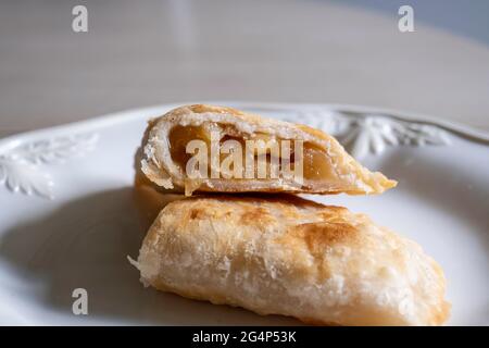Pastel de manzana frito casero cortado a la mitad a partir de manzanas secas con corteza de pastel escamoso sobre un plato blanco. Foto de stock