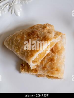 Pastel de manzana frito casero cortado a la mitad a partir de manzanas secas con corteza de pastel escamoso sobre un plato blanco. Foto de stock