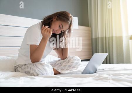 Hermosa mujer asiática tumbada y sonriendo la cama y su portátil. WFH Trabajando desde casa en cuarentena. Distanciamiento social Aislamiento propio Foto de stock
