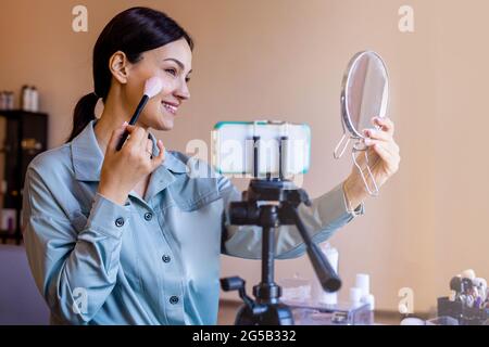Mujer visagist belleza blogger aplicación maquillaje uso cepillo y espejo de vídeo de disparo utilizar smartphone Foto de stock
