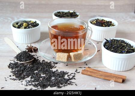 Surtido de té. Varios tipos de té en el tazón de fuente sobre el fondo rústico de madera. Té preparado en una taza de vidrio con azúcar. Foto de stock