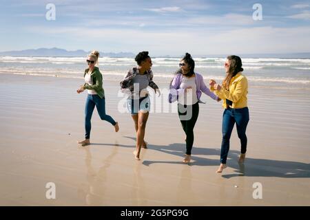 Feliz grupo de diversas amigas que se divierten, caminando por la playa y riéndose Foto de stock