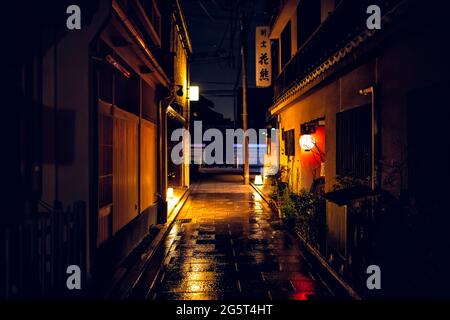 Kyoto, Japón - 16 de abril de 2019: Callejón vacío calle estrecha en el distrito de Gion por la noche con el exterior del restaurante y carretera húmeda después de la lluvia con foso Foto de stock