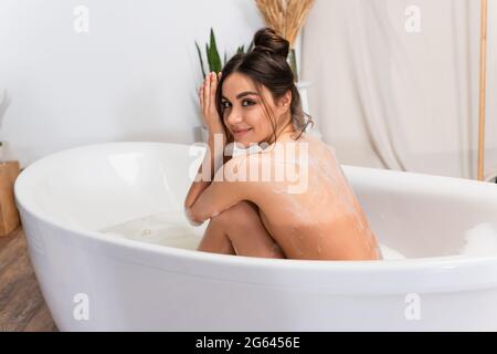 mujer joven mojada sentada en la bañera con espuma de baño Foto de stock