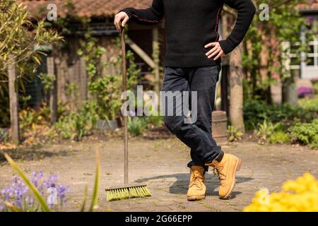 Un hombre jardinero que usa ropa informal limpiando las malezas de los  azulejos en su jardín de patio trasero mientras que está rodeado de flores  y plantas, relajante Fotografía de stock -