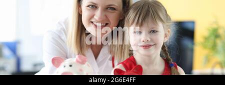 Mujer doctor y niña sosteniendo bancos piggy Foto de stock