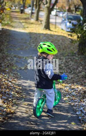 Abrace a un niño en su bicicleta de empuje en un casco verde Foto de stock