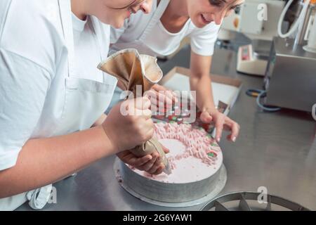 Confectioner women putting cream on cake finishing the pastry