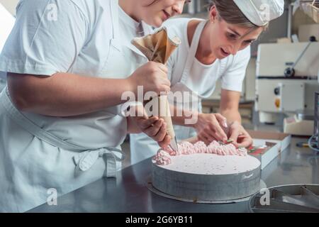 Confectioner women putting cream on cake finishing the pastry