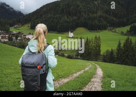 Mujer con mochila en camino de senderismo a la iglesia de San Johann en Val di Funes valle, Dolomitas, Italia, Europa