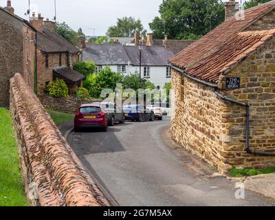 Vista de la calle en el pueblo de Wootton, Northampton, Reino Unido; antiguo granero de piedra a la derecha ahora convertido a uso residencial. Foto de stock