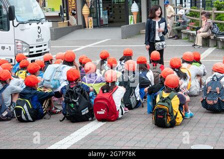 Grupo de estudiantes con los mismos sombreros brillantes y naranjas, con un maestro en un viaje de campo en Japón.