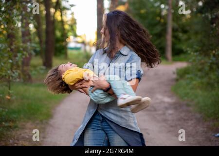 madre joven está girando con un bebé en sus brazos. mamá feliz bailando con niño en el fondo de la naturaleza y el bosque. mamá e hija ríen Foto de stock