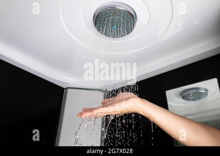 Una chica sostiene su mano sobre la presión del agua de una alcachofa de la ducha, cuarto de baño de la ducha de lluvia.