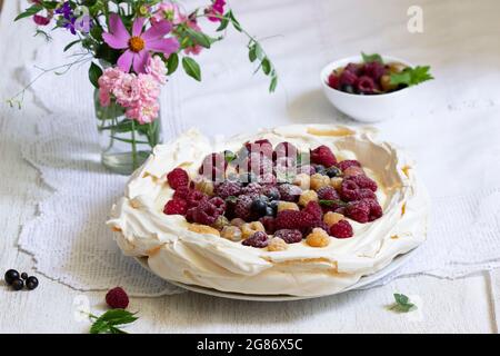 Pastel de Pavlova con crema y bayas y un ramo de flores sobre un fondo claro. Foto de stock