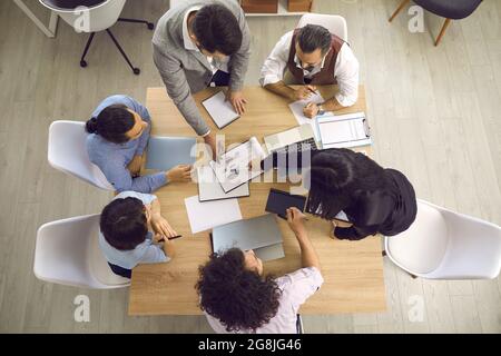 Vista superior de los empresarios que trabajan con ordenadores portátiles y documentos sentados en un escritorio. Foto de stock