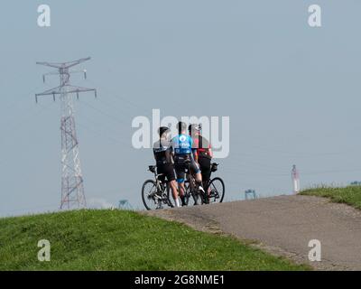 Doel, Bélgica, 21 de julio de 2021, tres ciclistas se están hablando unos con otros en la parte superior del dique en sus bicicletas Foto de stock