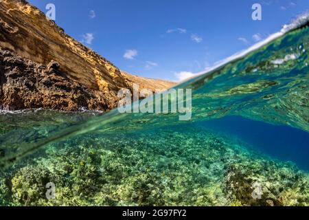 Una escena dividida con una ola que roza sobre un arrecife de coral duro y poco profundo debajo y el islote del cono volcánico de Molokina, en Hawaii. Este es un p. Marino estatal