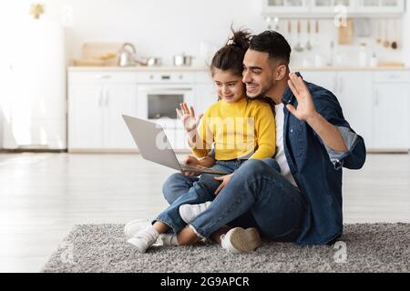 Papá árabe y mi hija pequeña haciendo videollamada con ordenador portátil en casa