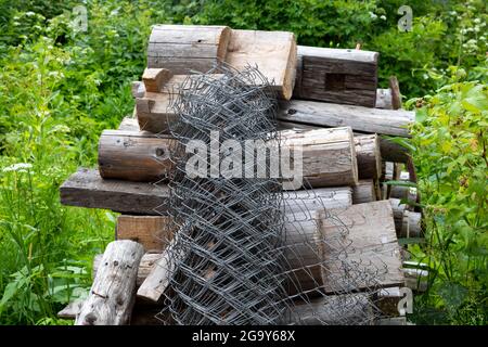 Un rollo de malla de alambre está cerca de un montón de troncos en el césped verde. Foto de stock