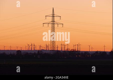 Pilones eléctricos y turbinas eólicas en el campo al atardecer; Biebesheim am Rhein, Hesse, Alemania Foto de stock