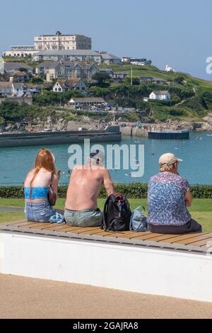 Los turistas se relajan bajo el sol en el Killacourt mirando hacia el Atlantic Hotel en Newquay en Cornwall. Foto de stock
