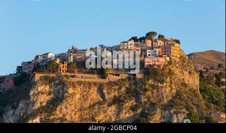 Taormina, Messina, Sicilia, Italia. Vista al bonito pueblo medieval de Castelmola, el amanecer, casas precariamente encaramadas aferradas a la cima del acantilado. Foto de stock